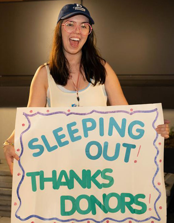 Covenant House Sleep Out volunteer holding sign that reads "SLEEPING OUT! THANKS DONORS!"