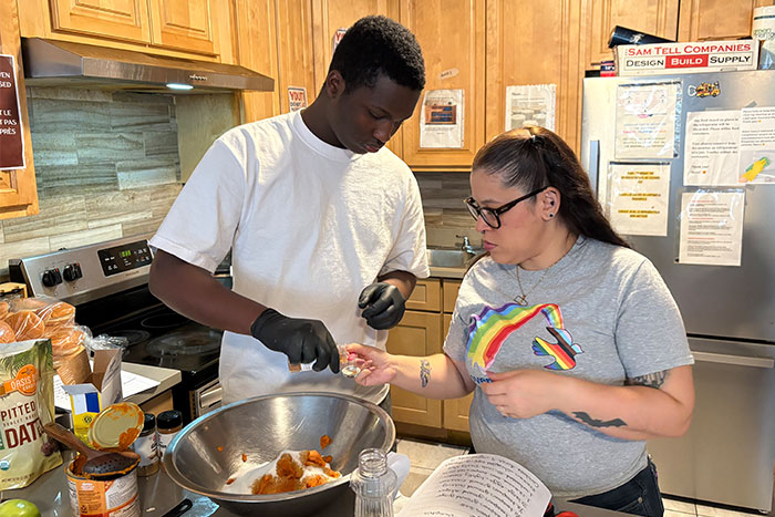 Covenant House staff Daisy with former homeless boy cooking in kitchen