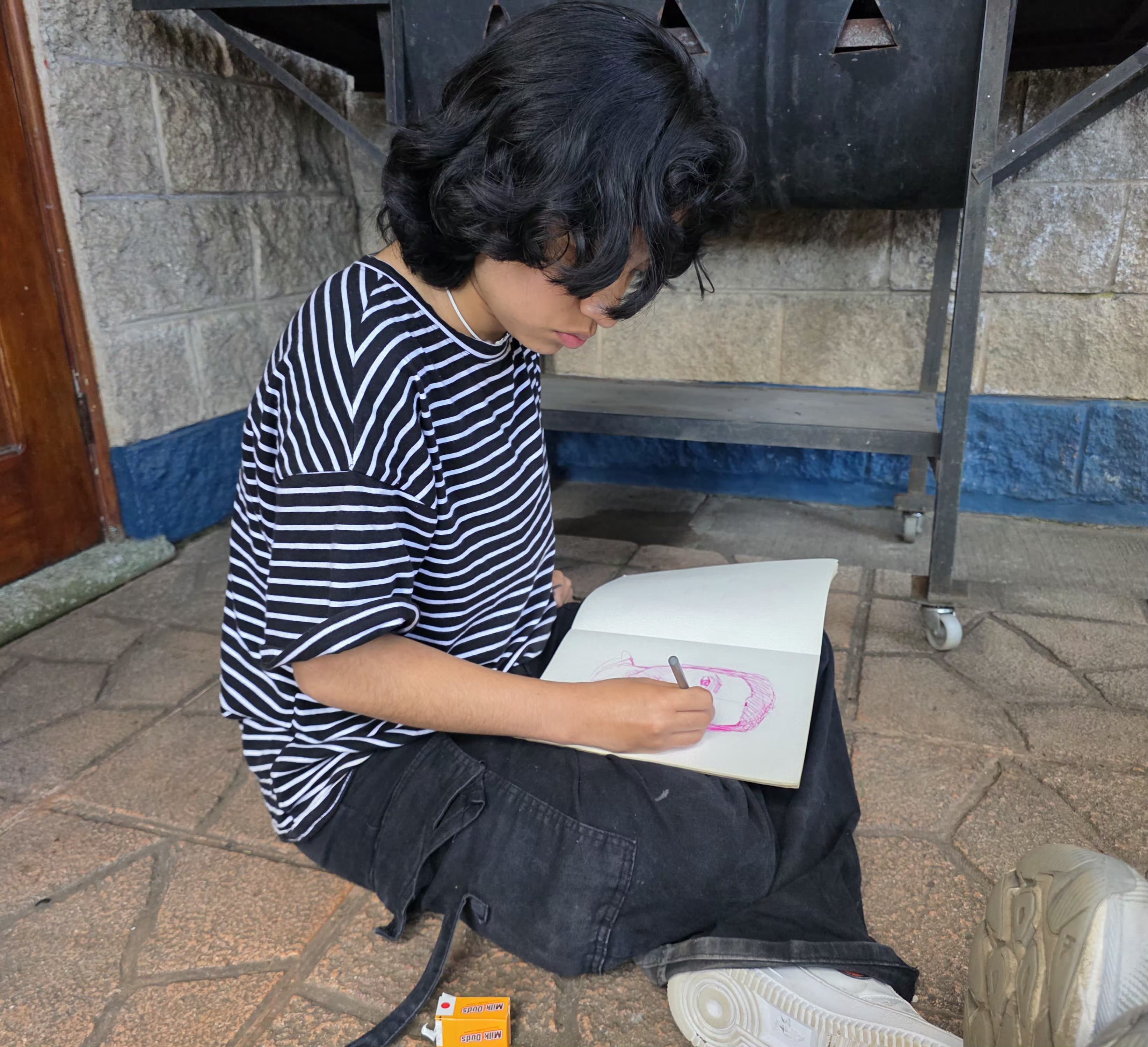 Mateo from Covenant House Guatemala sits on the ground and creates artwork in their notebook.
