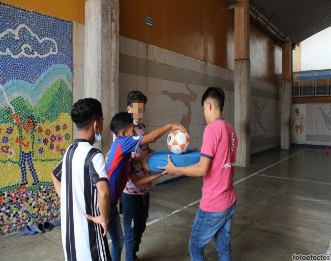 Four residents from Covenant House Honduras playing with a football in a recreation center/gymnasium.