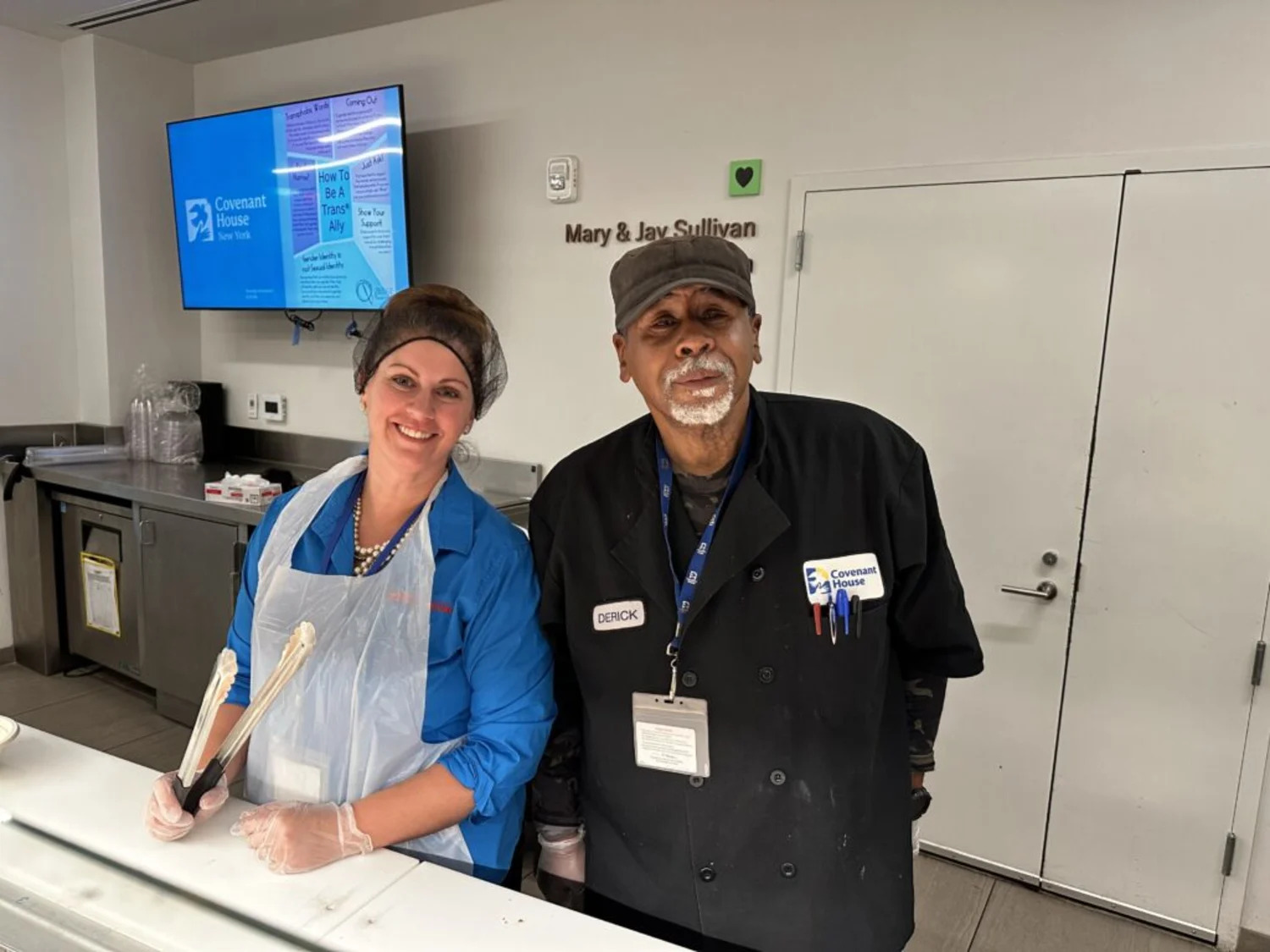 Two members of the kitchen staff at Covenant House posing for a photo behind the cafeteria counter.
