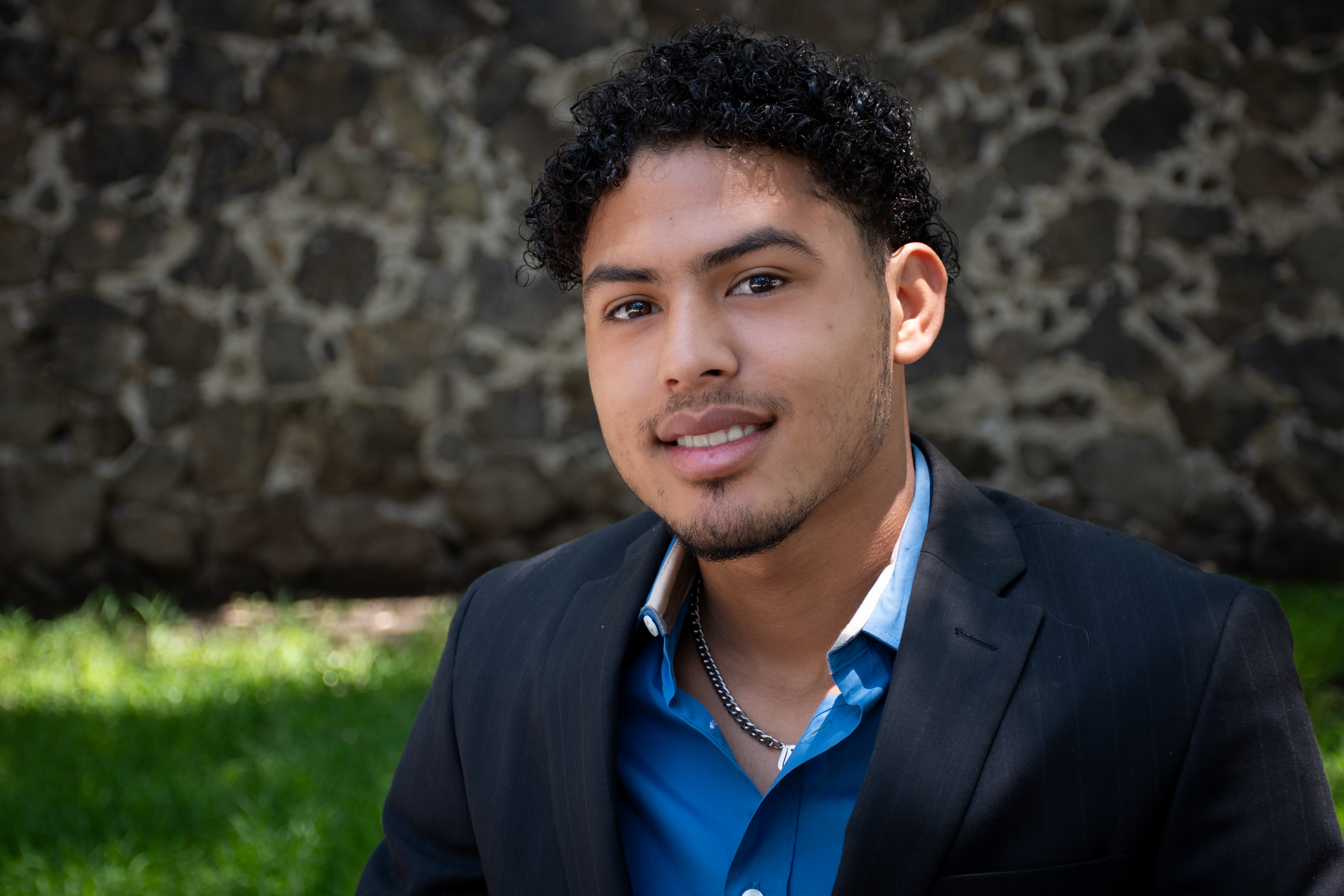 Close-up shot of Jonathan, who resides in Covenant House Mexico’s independent living program, posing seated outside in front of a stone wall.