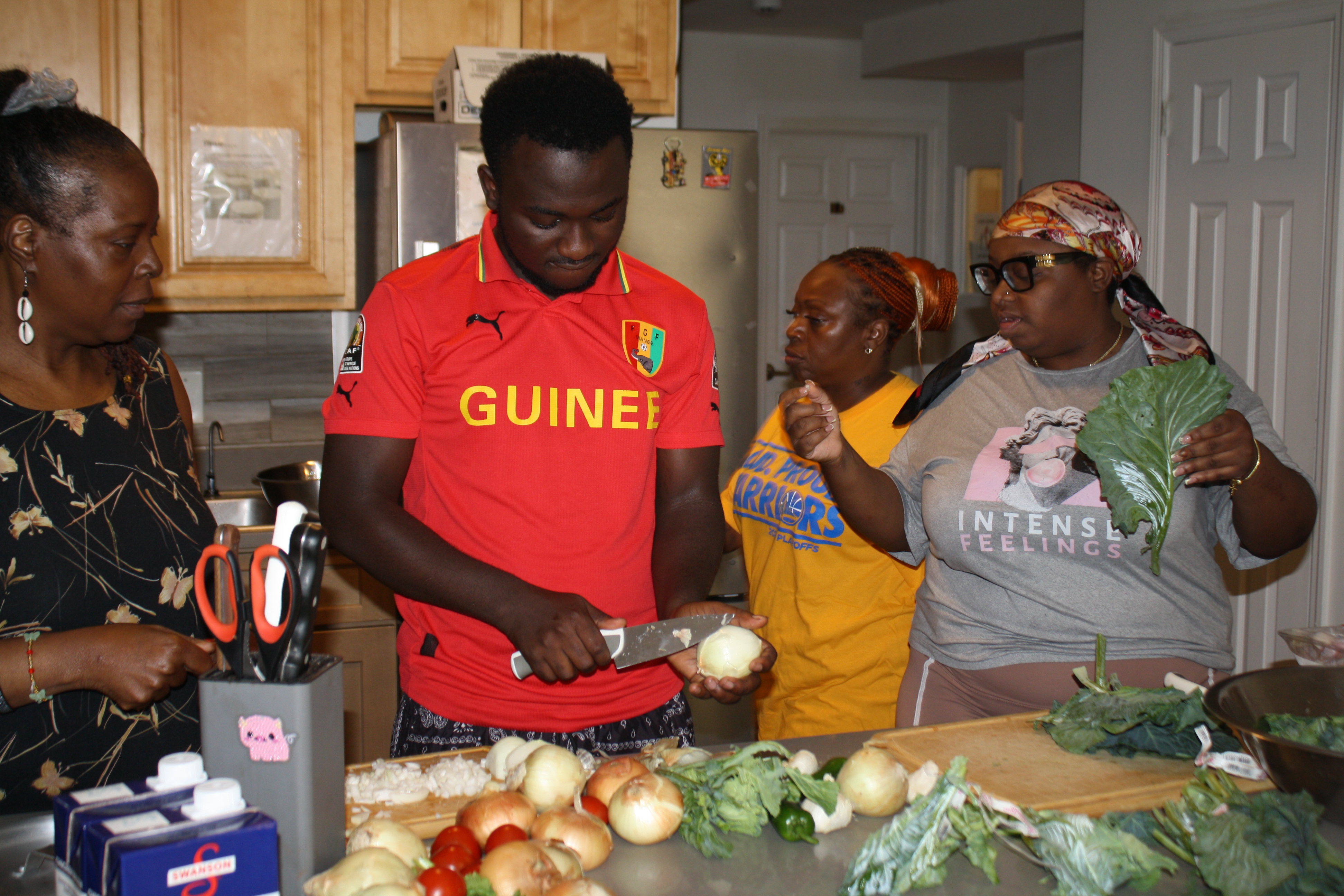A Covenant House staff member and several residents in a shelter kitchen prepping ingredients and cutting onions as they prepare to cook recipes sent to them from supporters.