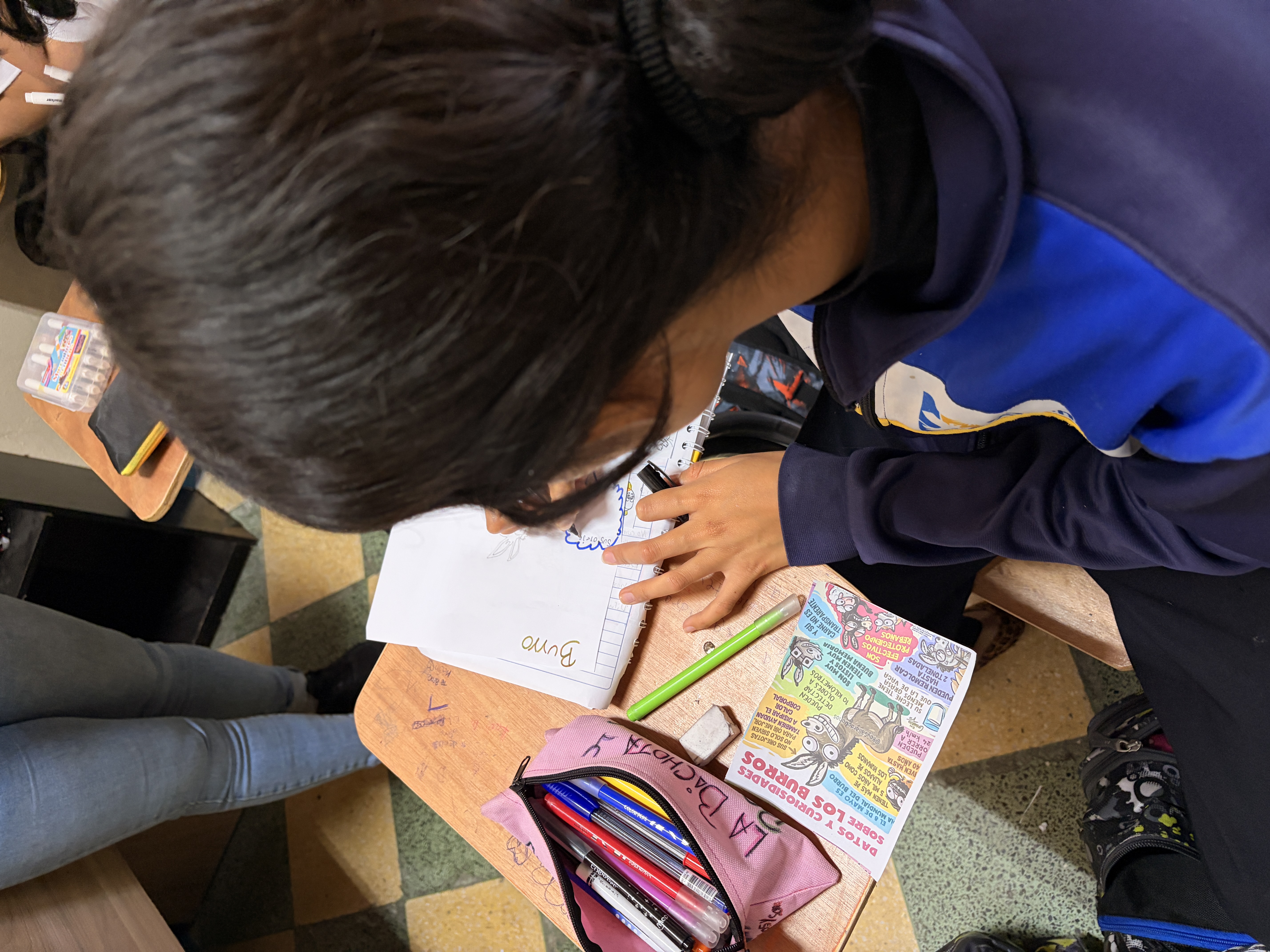 At her desk, Covenant House Guatemala resident Lucy uses colored pencils to write and illustrate a story in her notebook.