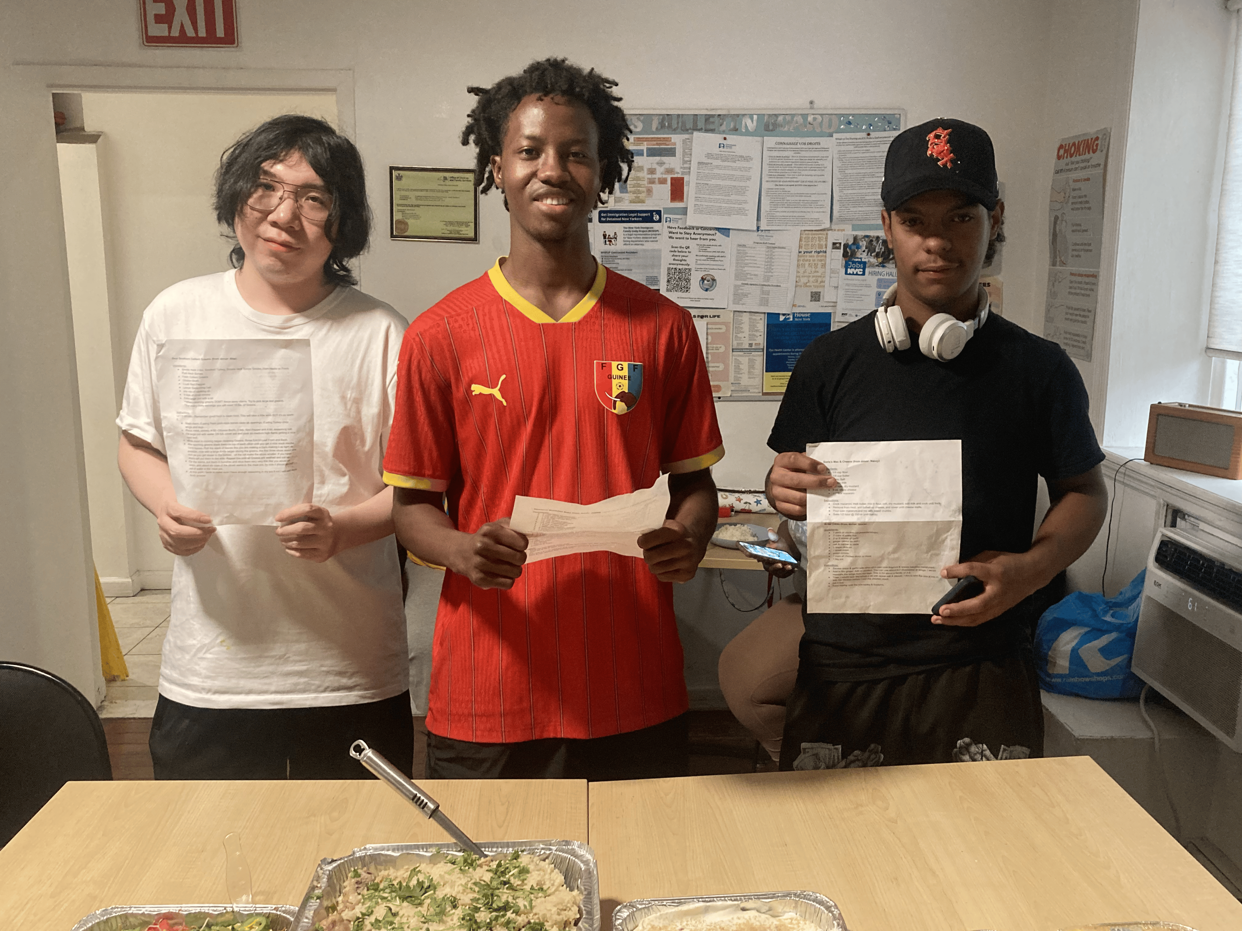 Three Covenant House residents in a kitchen displaying recipes sent to them from supporters.
