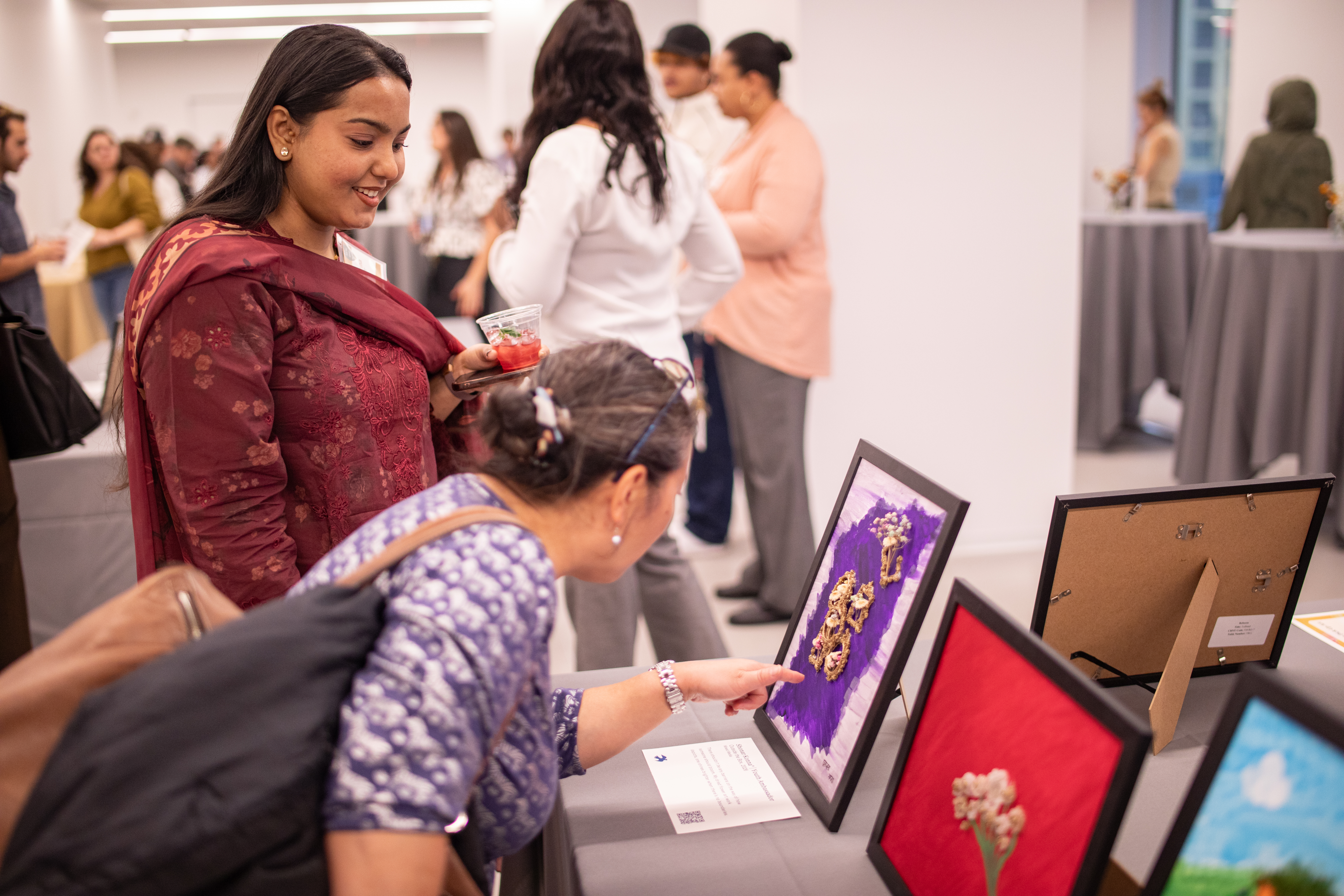 Youth artist stands by as an art patron examines a piece the youth created, which stands, with other pieces, on a table at the fourth annual CHNY Youth Art Show.
