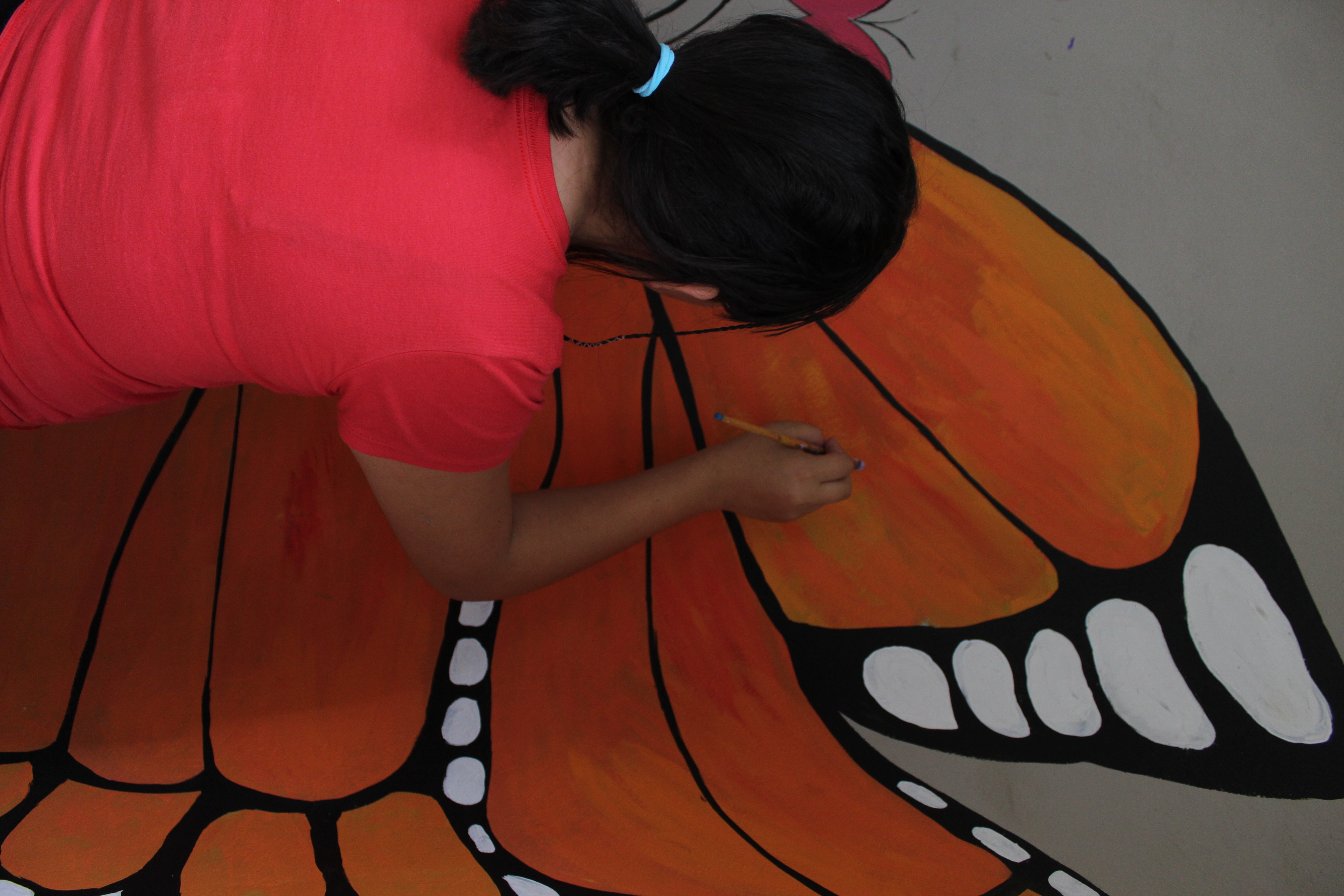 Young girl paints a butterfly mural at Covenant House Honduras.