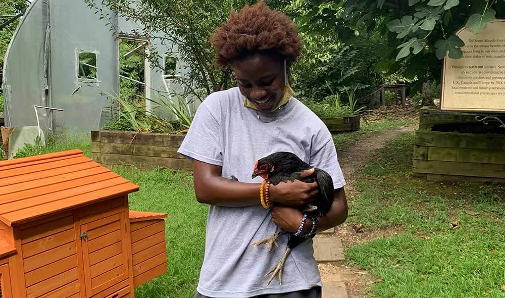 Covenant House resident Ann holding a chicken in a yard