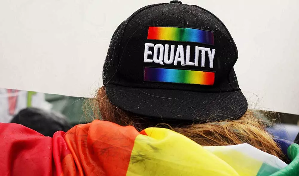 Person at Pride wearing LGBTQ+ flag and equality hat | Covenant House