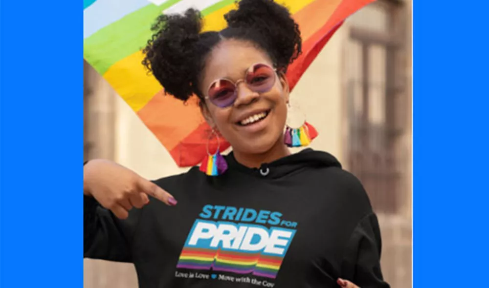 LGBTQ+ youth wearing strides for pride hoodie with LGBTQ+ flag flowing behind