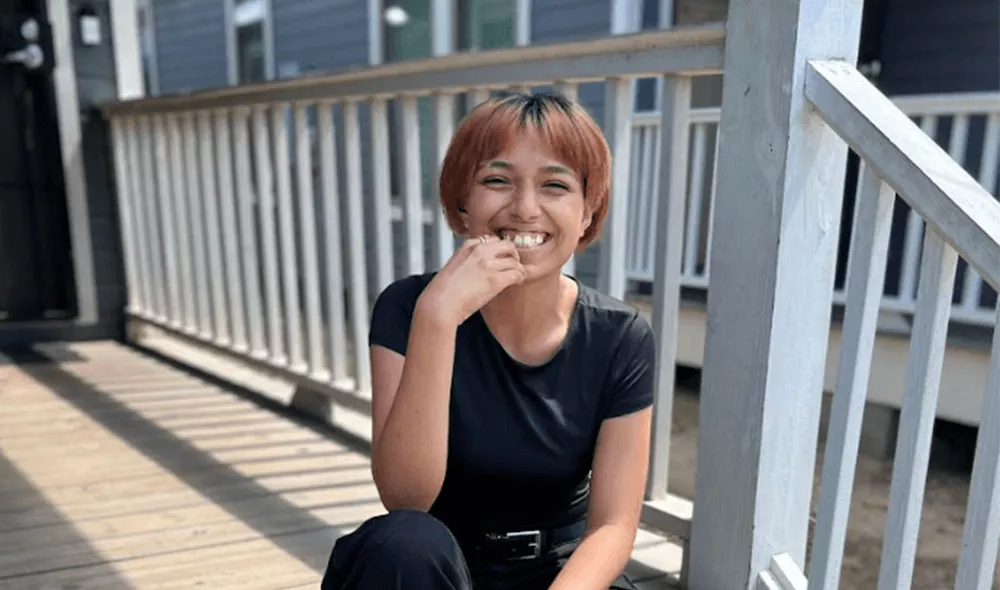 Covenant House Texas resident and homeless youth Alexis smiling and sitting on a wood deck