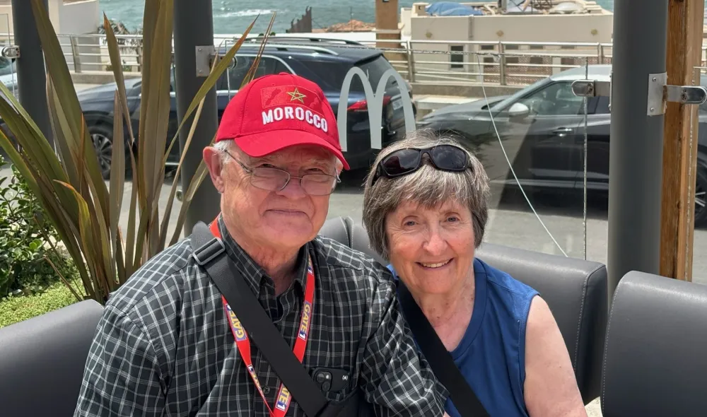 Tom and Mary O'Neill (respectively), Covenant House donors, pose smilingly for a photo while seated outdoors with the ocean behind them.