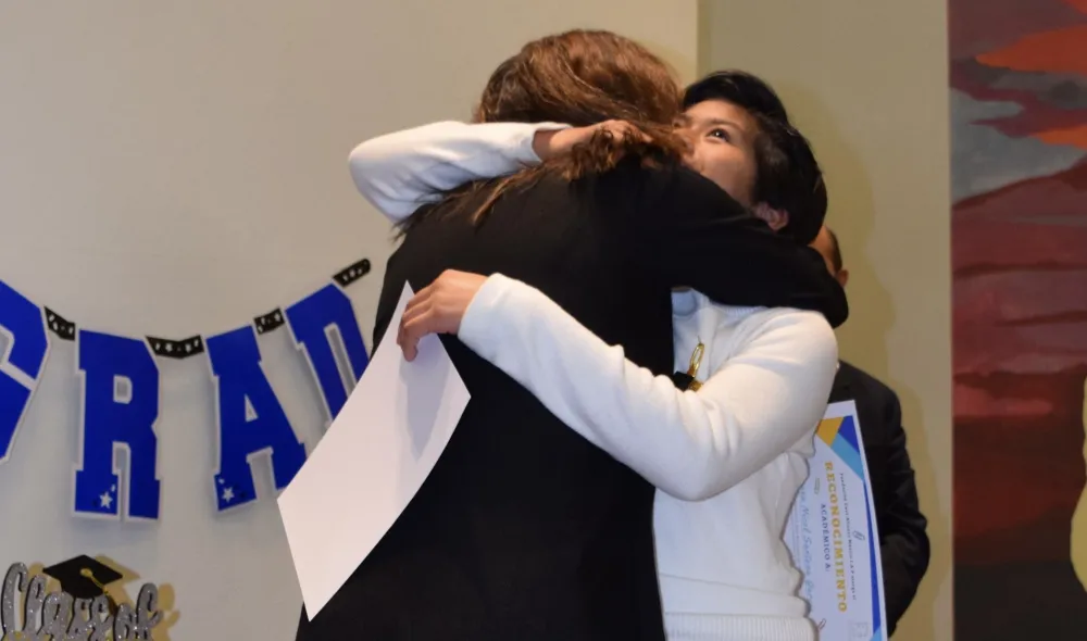 A student and a school staff member hug and celebrate at a graduation ceremony.
