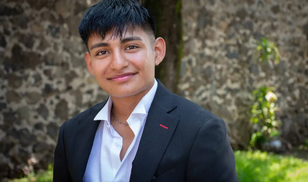 Close-up photo of Edwin at Covenant House Mexico, surrounded by greenery and a stone wall.