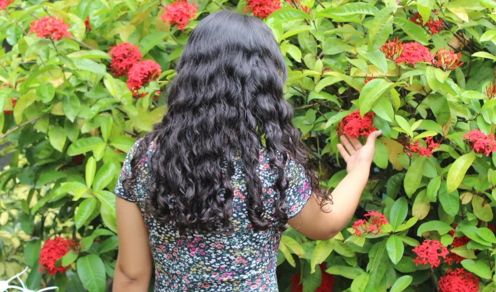 Covenant House Honduras resident Sofia stands, back turned, in a garden of red flowers.
