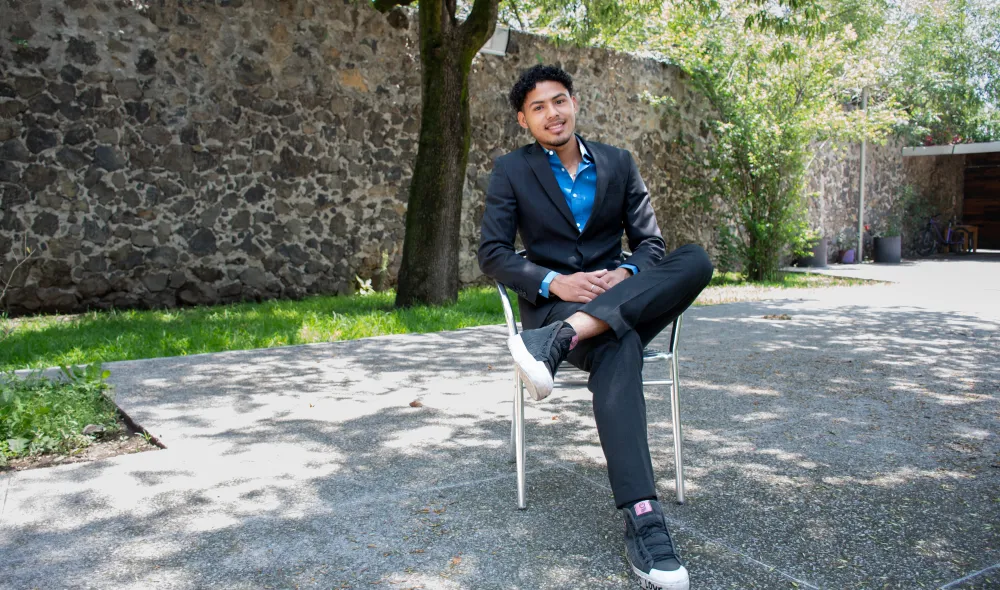 Medium shot of Jonathan, who resides in Covenant House Mexico’s independent living program, posing seated outside in front of a stone wall.