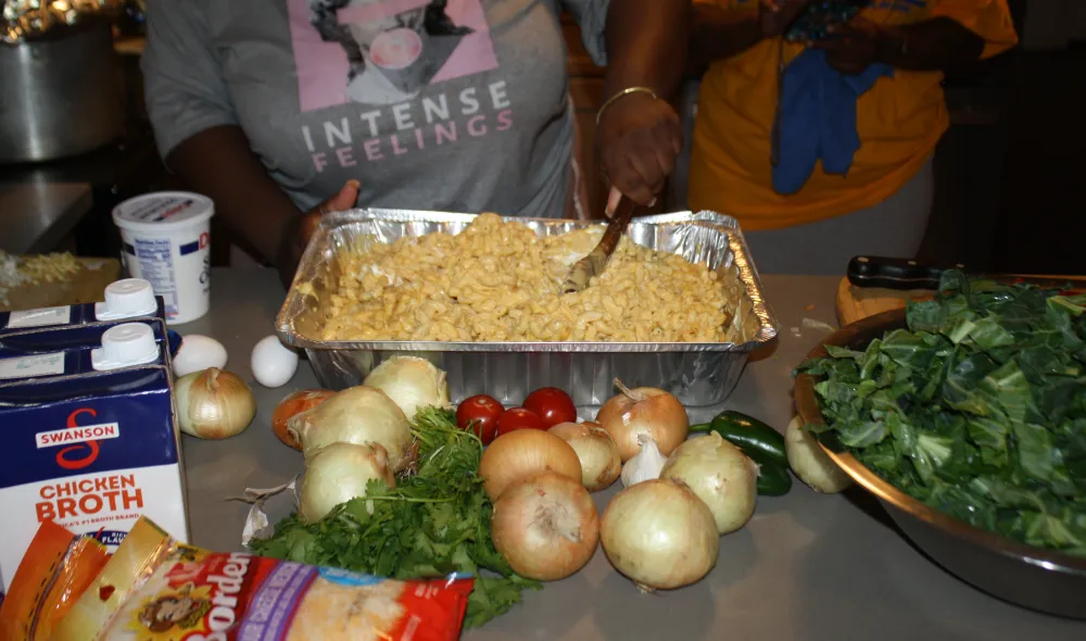 Residents of Covenant House display a finished tray of macaroni and cheese as well as other ingredients from a recipe share.
