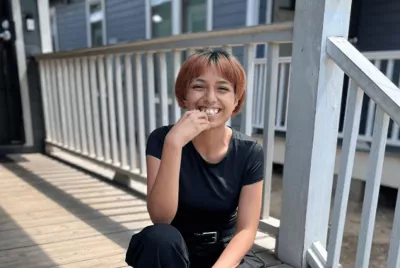 Covenant House Texas resident and homeless youth Alexis smiling and sitting on a wood deck