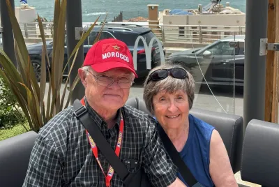 Tom and Mary O'Neill (respectively), Covenant House donors, pose smilingly for a photo while seated outdoors with the ocean behind them.