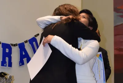 A student and a school staff member hug and celebrate at a graduation ceremony.