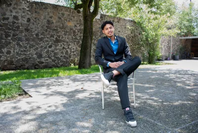Medium shot of Jonathan, who resides in Covenant House Mexico’s independent living program, posing seated outside in front of a stone wall.
