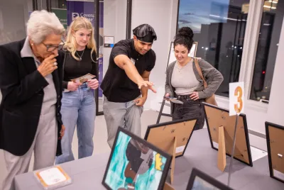 CHNY youth artist in beret explains a piece of art he created to patrons standing around a table with various works.