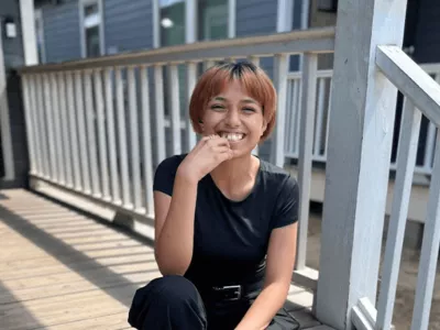 Covenant House Texas resident and homeless youth Alexis smiling and sitting on a wood deck