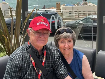 Tom and Mary O'Neill (respectively), Covenant House donors, pose smilingly for a photo while seated outdoors with the ocean behind them.