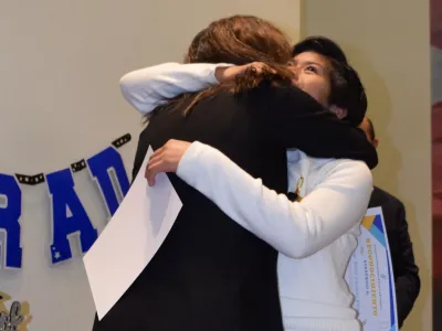 A student and a school staff member hug and celebrate at a graduation ceremony.