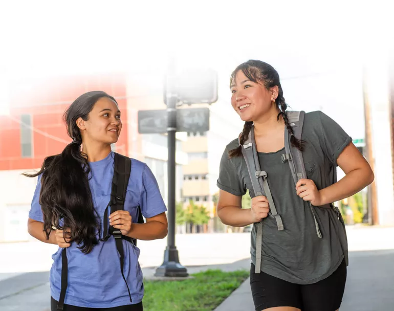 Two young ladies with backpacks walking and talking.