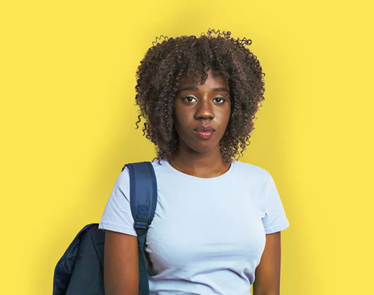 youth with backpack standing in front of yellow background