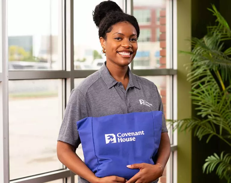 Smiling Covenant House staff member holding Covenant House tote | immediate care and shelter for homeless youth | Workplace Giving - Employee Giving - Employee Giving Programs