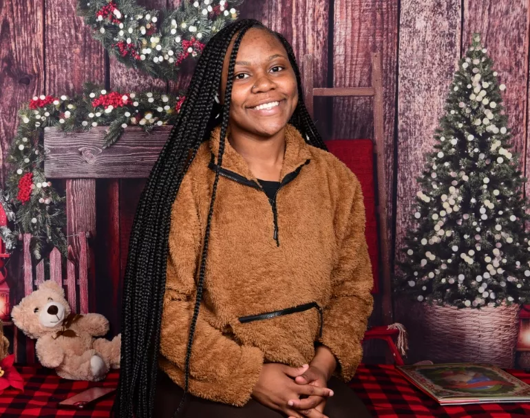 Bring Joy to Homeless Youth - Image of former homeless teen in front of Christmas decorations | Covenant House - Donate Now