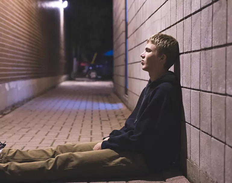 Young homeless man leaning against a wall