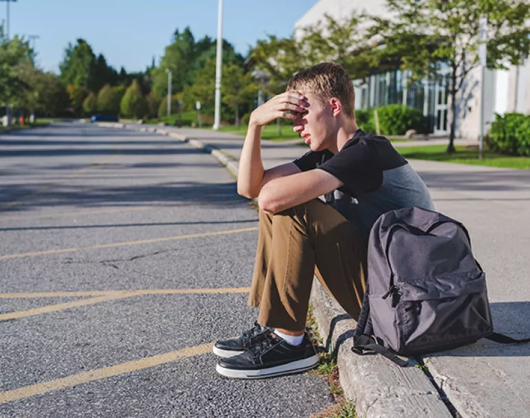 homeless teenage boy sitting on sidewalk | Donate today to support trafficked youth and homeless kids